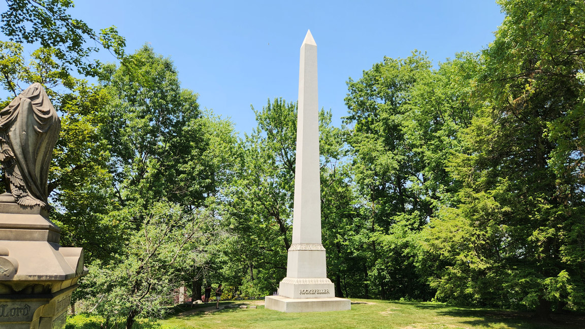 Photograph of the Rockefeller Obelisk at Lake View Cemetery, showing the tall granite monument rising above the surrounding landscape